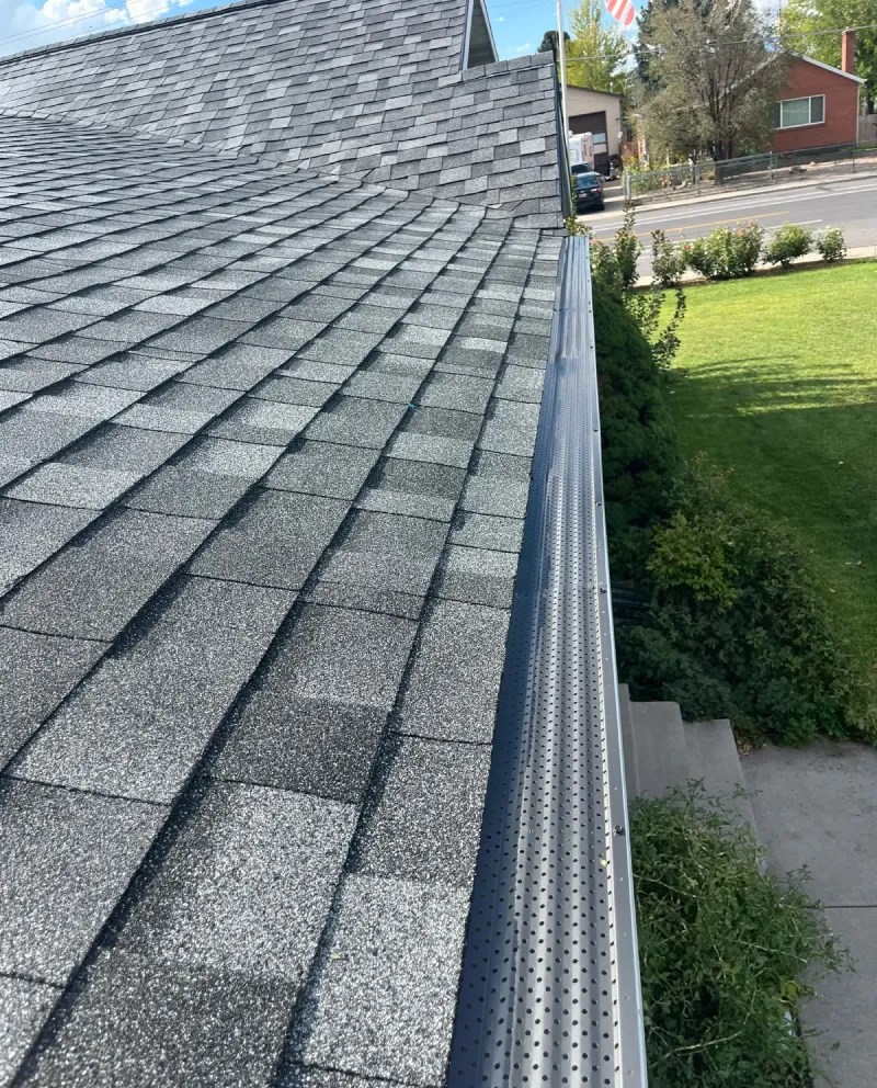 roofline of a house with gray asphalt shingles green lawn visible below